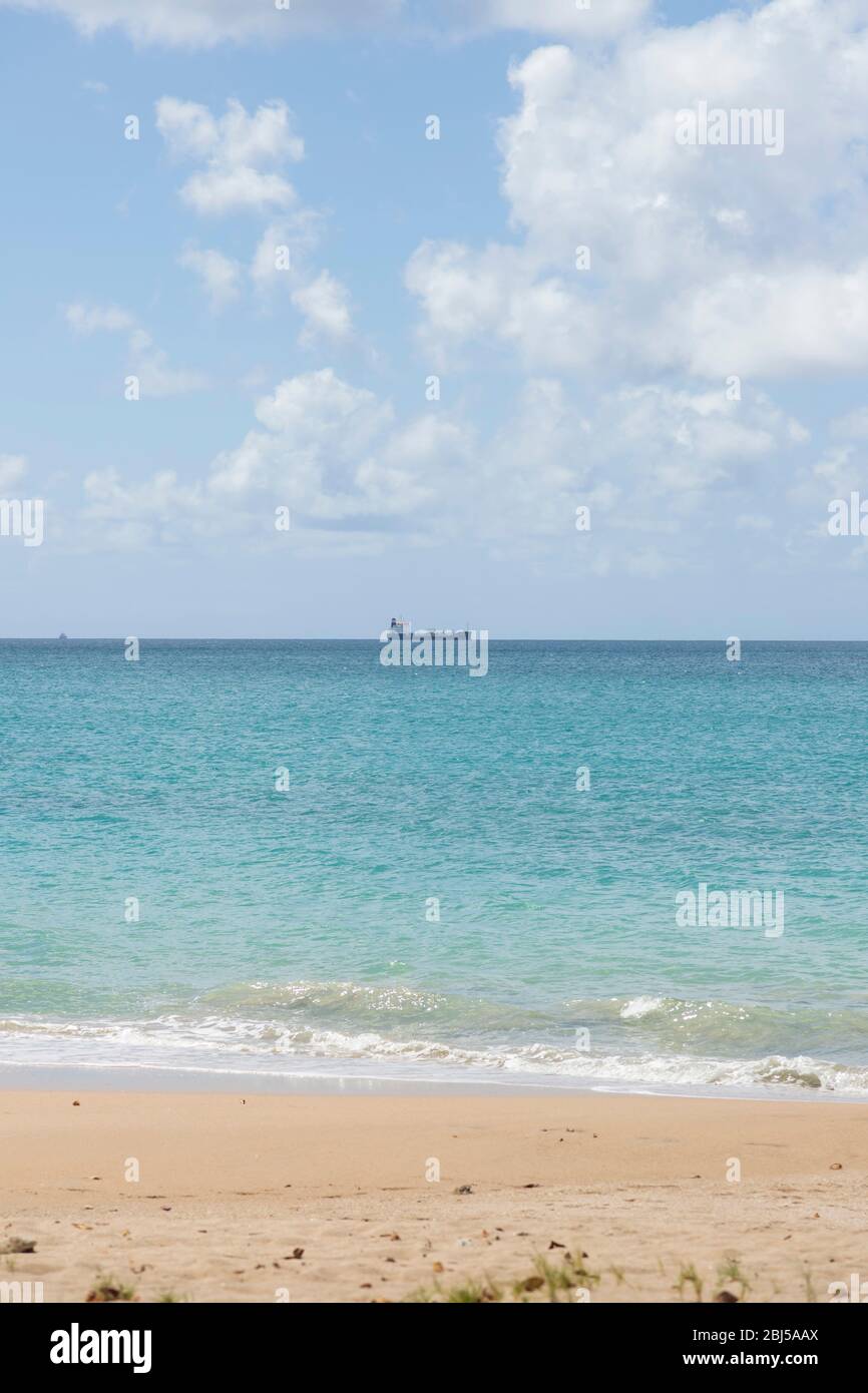 Foto vom Strand in Porträtausrichtung an einem hellen sonnigen Tag mit einem Frachtschiff im Hintergrund am Horizont Stockfoto