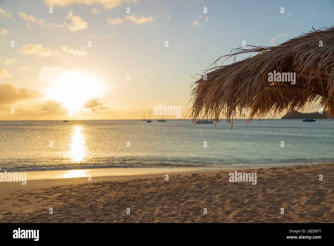Licht reflektiert auf dem Wasser, als die Sonne nahe dem Horizont erreicht und das Ende eines anderen Tages an einem Urlaubsstrand signalisiert Stockfoto
