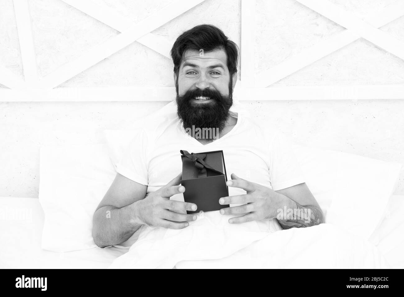 Schauen gut. Am frühen Morgen überraschen. Beginnen Sie den Tag mit Geburtstag. Geschenk für verbrachte Nacht. bärtiger Mann Urlaub zuhause verbringen. Valentines Tag. Besonderes Geschenk. happy Hipster mit vorhanden, im Bett. Stockfoto