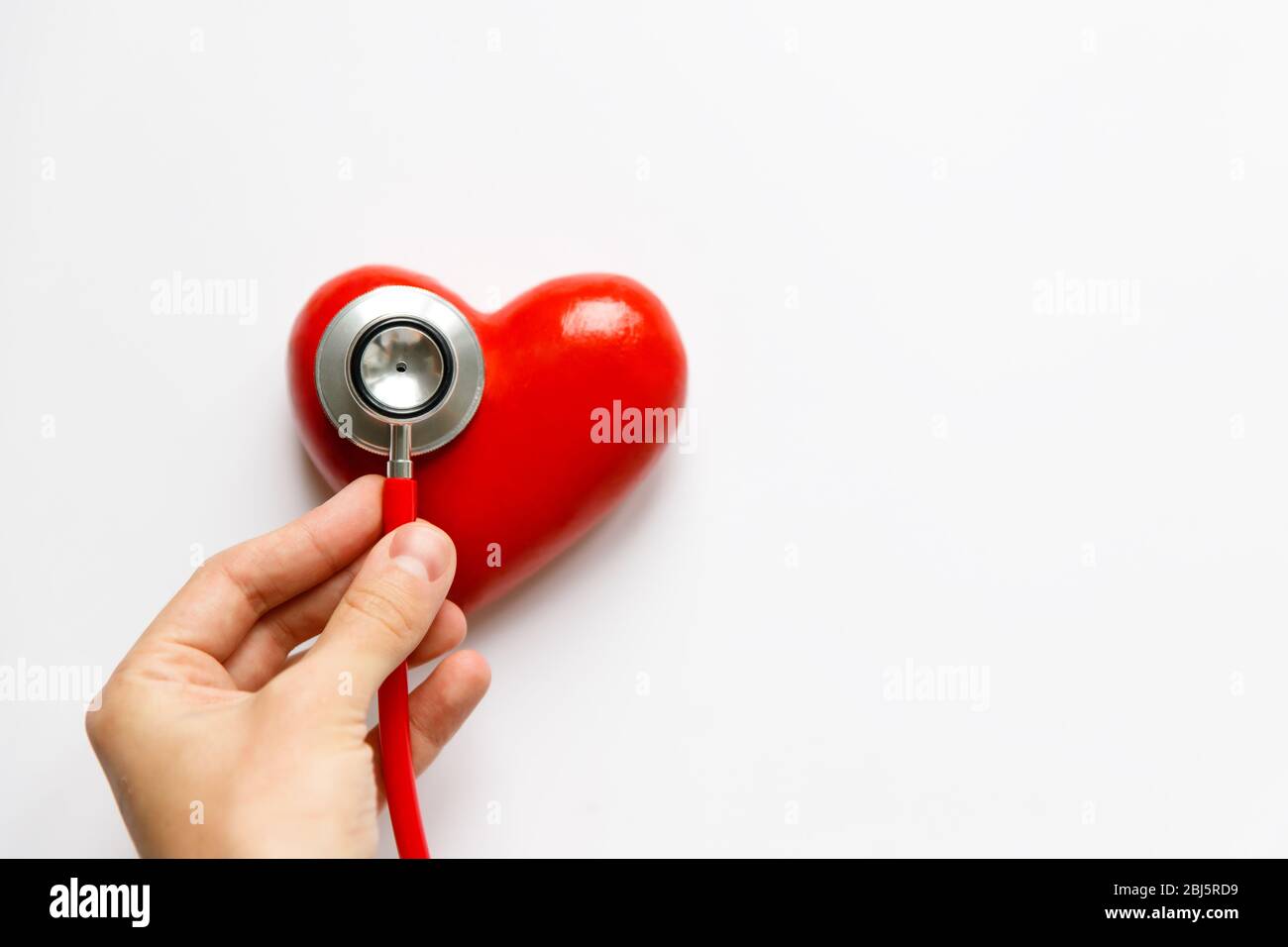 Nahaufnahme der Hand des Menschen, die ein rotes Stethoskop am Herzen hält - medizinisches Diagnosegerät für Auskultation (Hören) von Klängen, die vom Herzen kommen, bronc Stockfoto