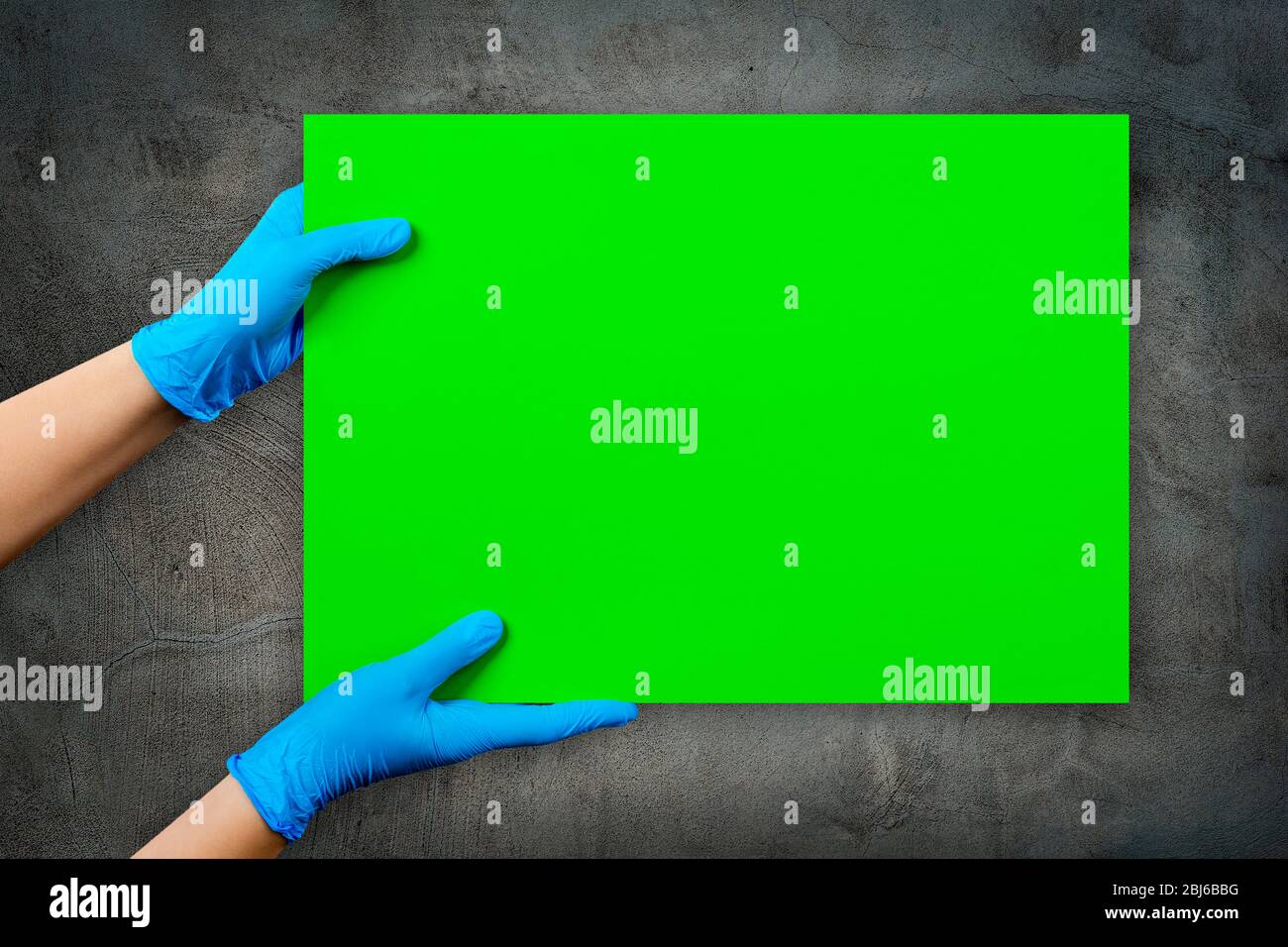 Leere grüne Karte in Arzthand in blauen Handschuhen mit Kopierraum, auf grauer Zementmörtel-Wand. Stockfoto