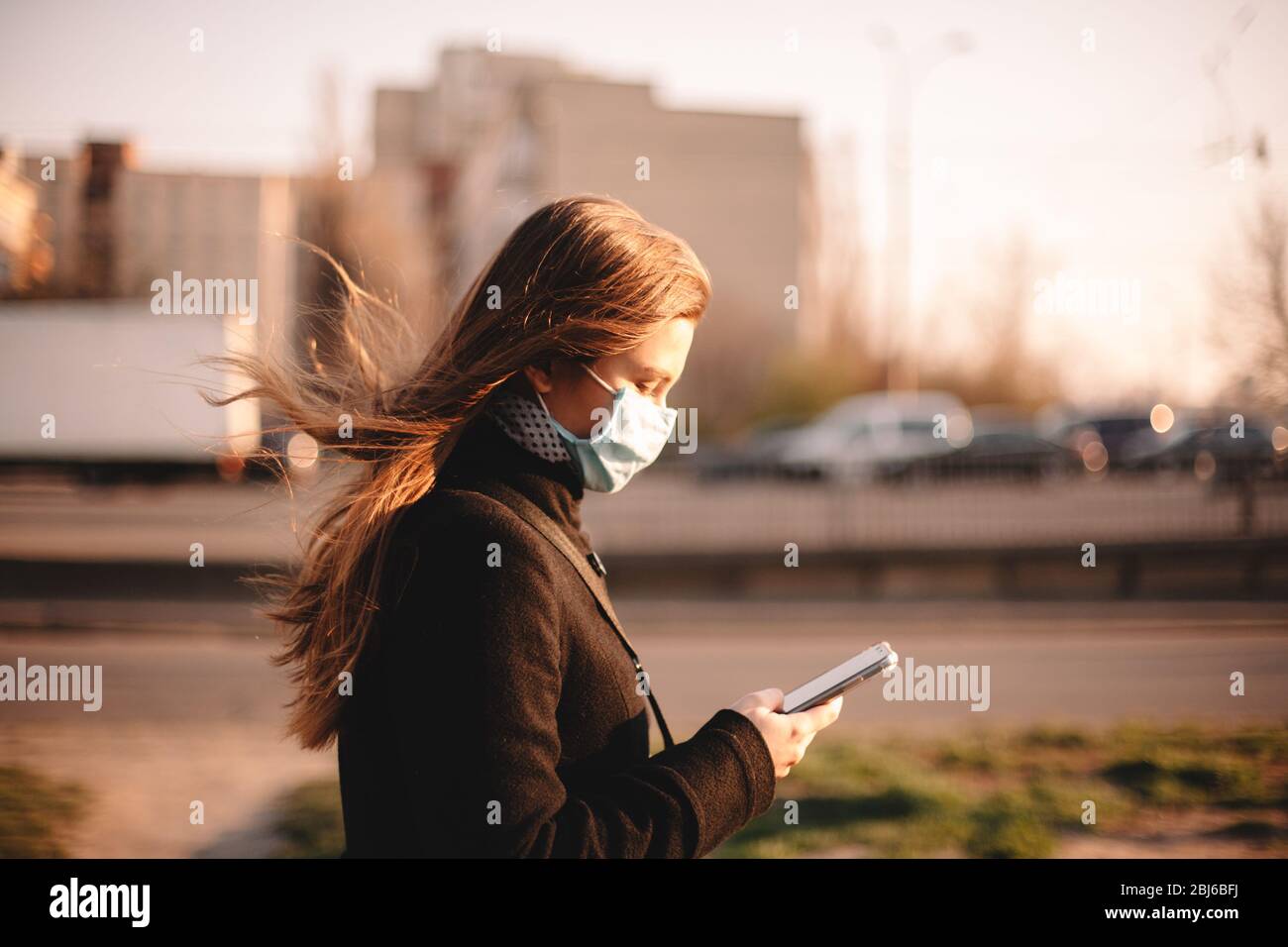 Junge Frau trägt schützende Gesicht medizinische Maske, während mit Smartphone zu Fuß auf der Straße in der Stadt Stockfoto