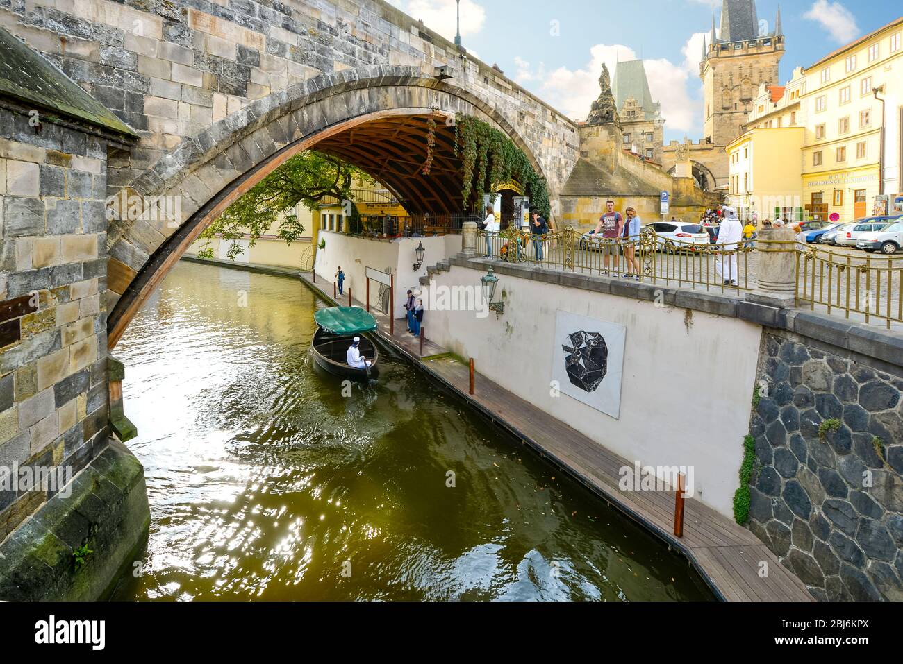 Ein Kanal mit einem Touristenboot unter einer Brücke auf der Kampa Insel in Prag, Tschechien mit dem Brückenturm der Kleinseite in der Ferne Stockfoto