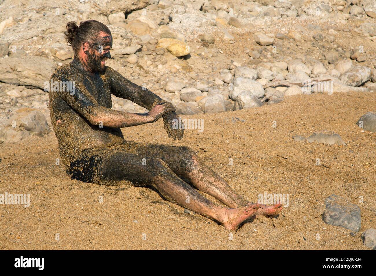 Ein Mann, der natürlichen Schlammsammel aufbringt und die Natur am Strand des Toten Meeres genießt Stockfoto