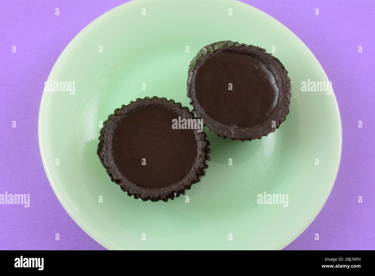 Zwei dunkle Schokoladen-Torten mit Schokoladenkrusten in Pappbechern auf grünem Dessertteller Stockfoto