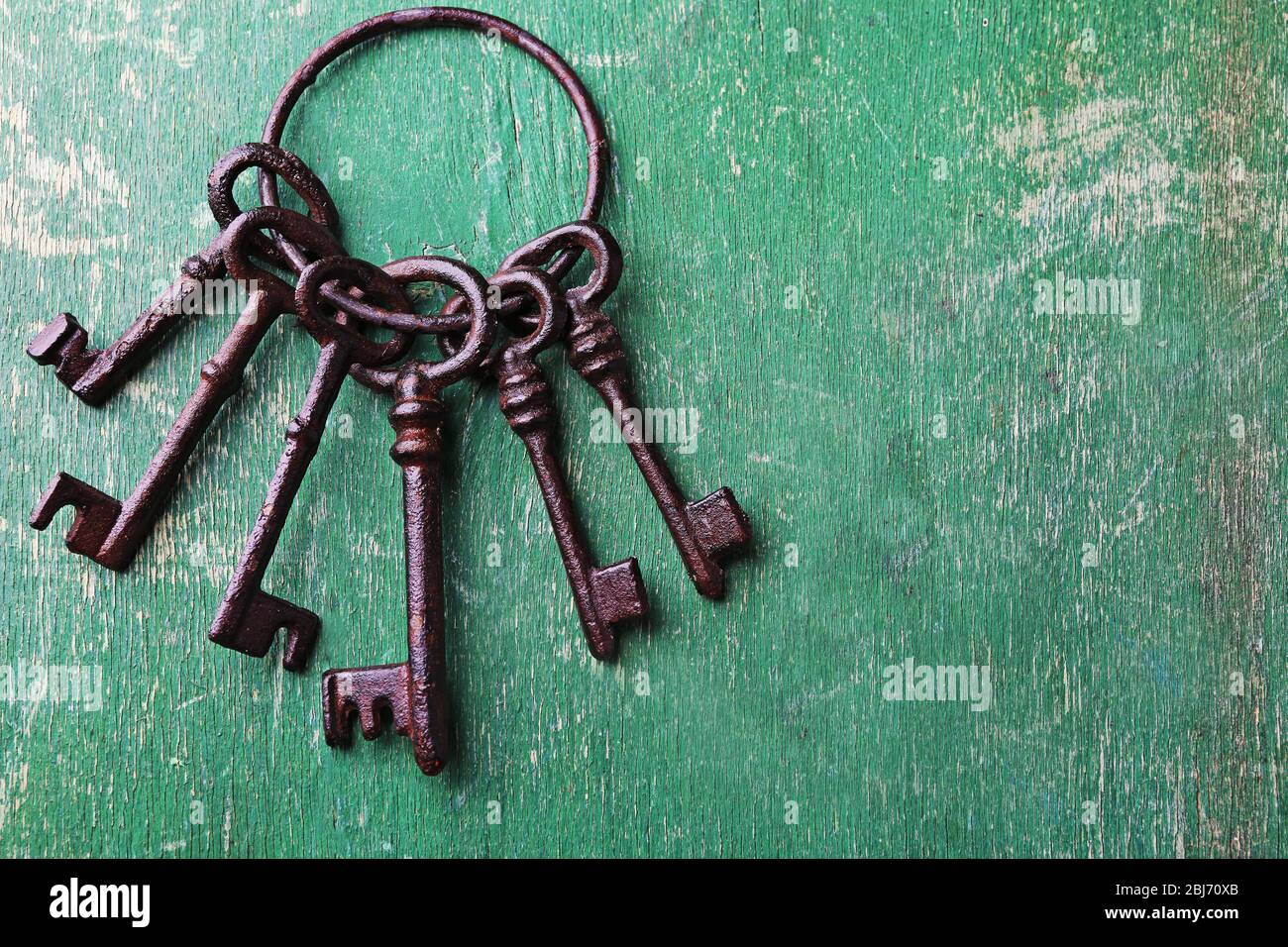 Ein Haufen alter Schlüssel auf grün verkratztem Holzhintergrund, Nahaufnahme Stockfoto
