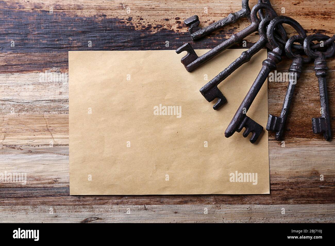 Ein Haufen alter Schlüssel mit leerem Blatt Papier auf Holzhintergrund, Nahaufnahme Stockfoto