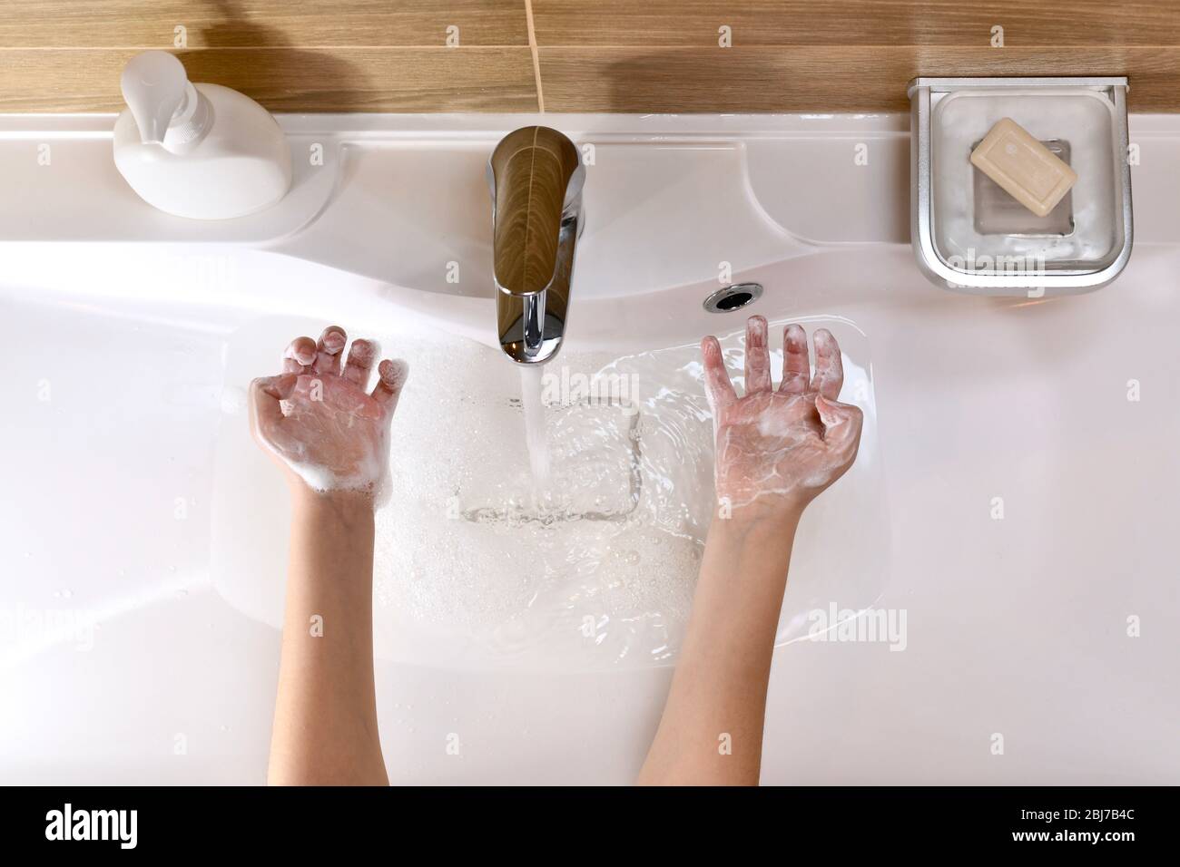 Das Kind zeigt die Handflächen, die mit Seifenschaum gefüllten Händen mit gebogenen Fingern über dem Waschbecken mit Wasser gegossen werden. Stockfoto