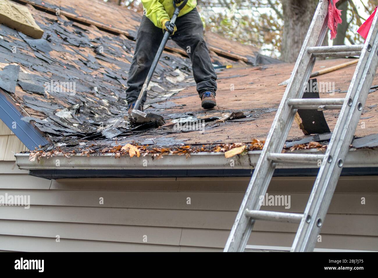 Arbeiter verwenden Spezialwerkzeuge, um alte Schindeln aus einem Zuhause zu entfernen Stockfoto