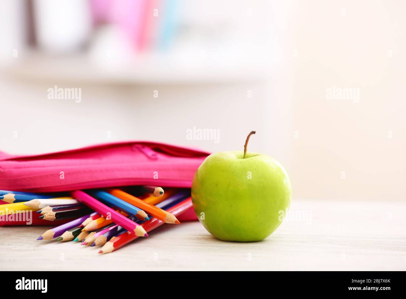 Apfel und Bleistiftbox voll mit Bleistiften auf dem Tisch im Zimmer Stockfoto