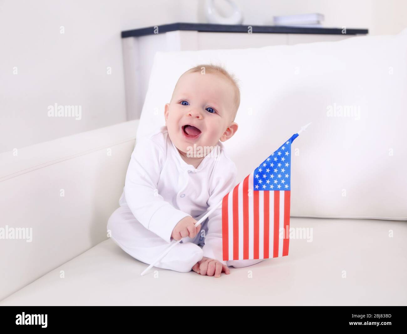 Niedlicher Junge auf weißer Couch mit amerikanischer Flagge, Nahaufnahme Stockfoto