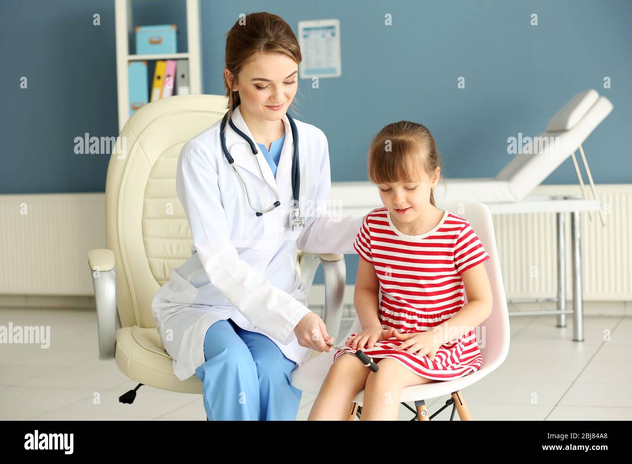 Doktor, das Mädchen mit einem Reflexhammer im Büro untersucht Stockfoto