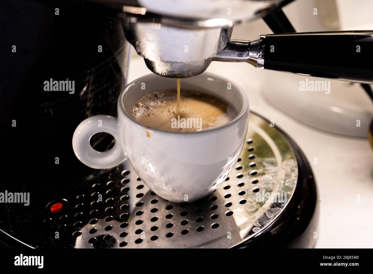Nahaufnahme des italienischen schwarzen Kaffees, der morgens aus einer Kaffeemaschine in eine Cappuccino-Tasse tropft Stockfoto