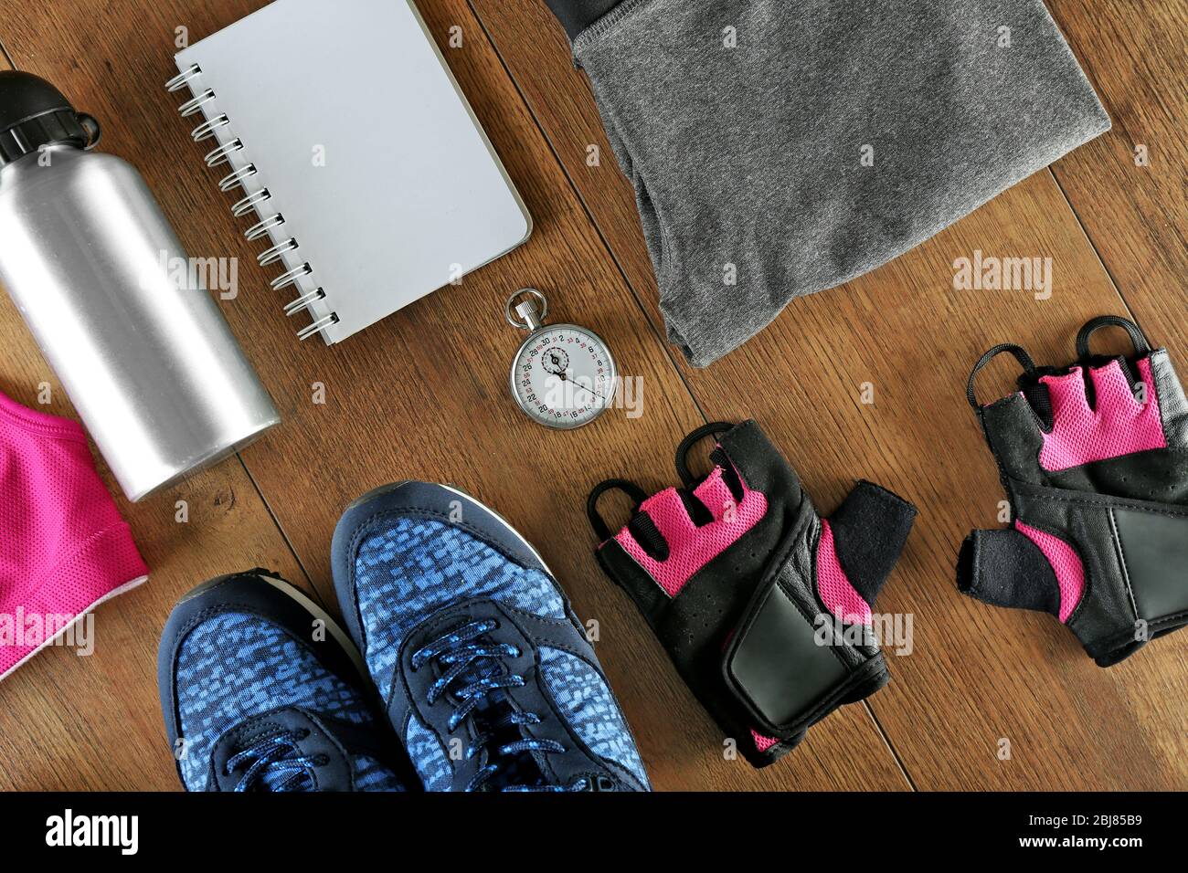 Athletenset mit Damenbekleidung, Wasserflasche, Stoppuhr und Notizbuch auf Holzhintergrund Stockfoto