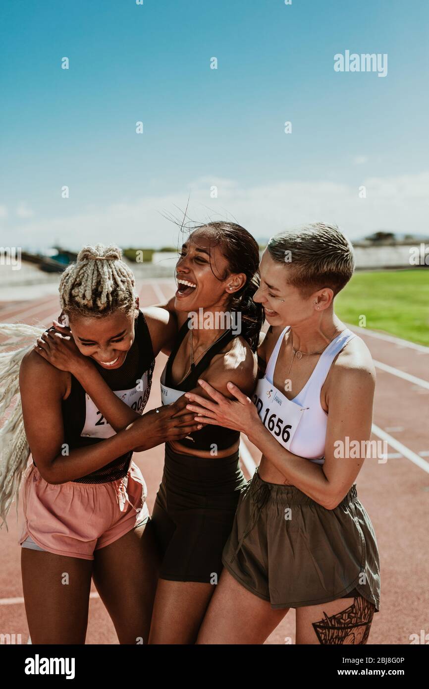 Läuferinnen feiern den Sieg, umarmen sich gegenseitig und lachen auf der Strecke. Sportfrauen gratulieren einander, nachdem sie das Rennen gewonnen haben. Stockfoto