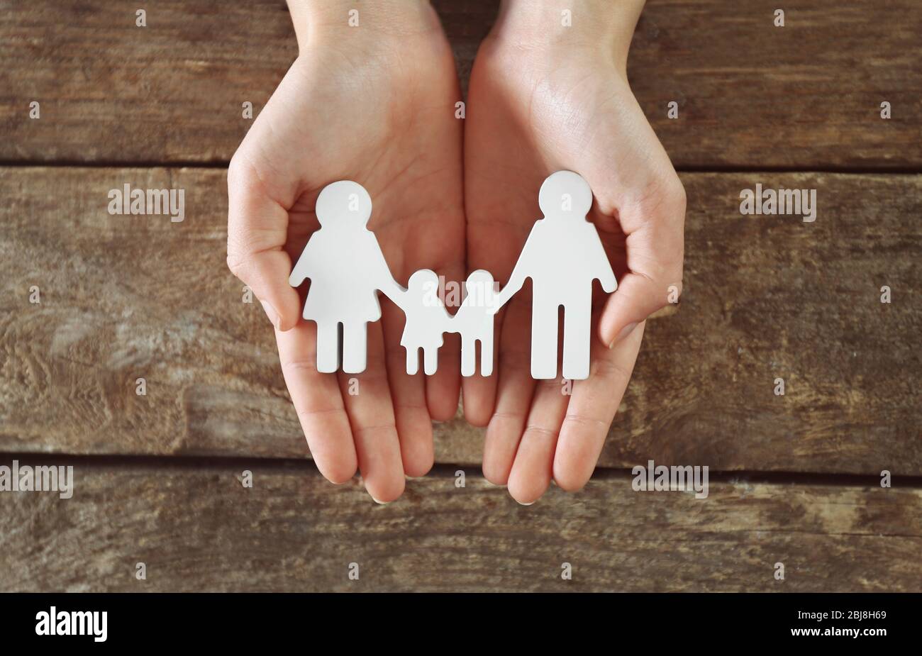 Weibliche Hände halten Familienfigur auf Holzhintergrund Stockfoto
