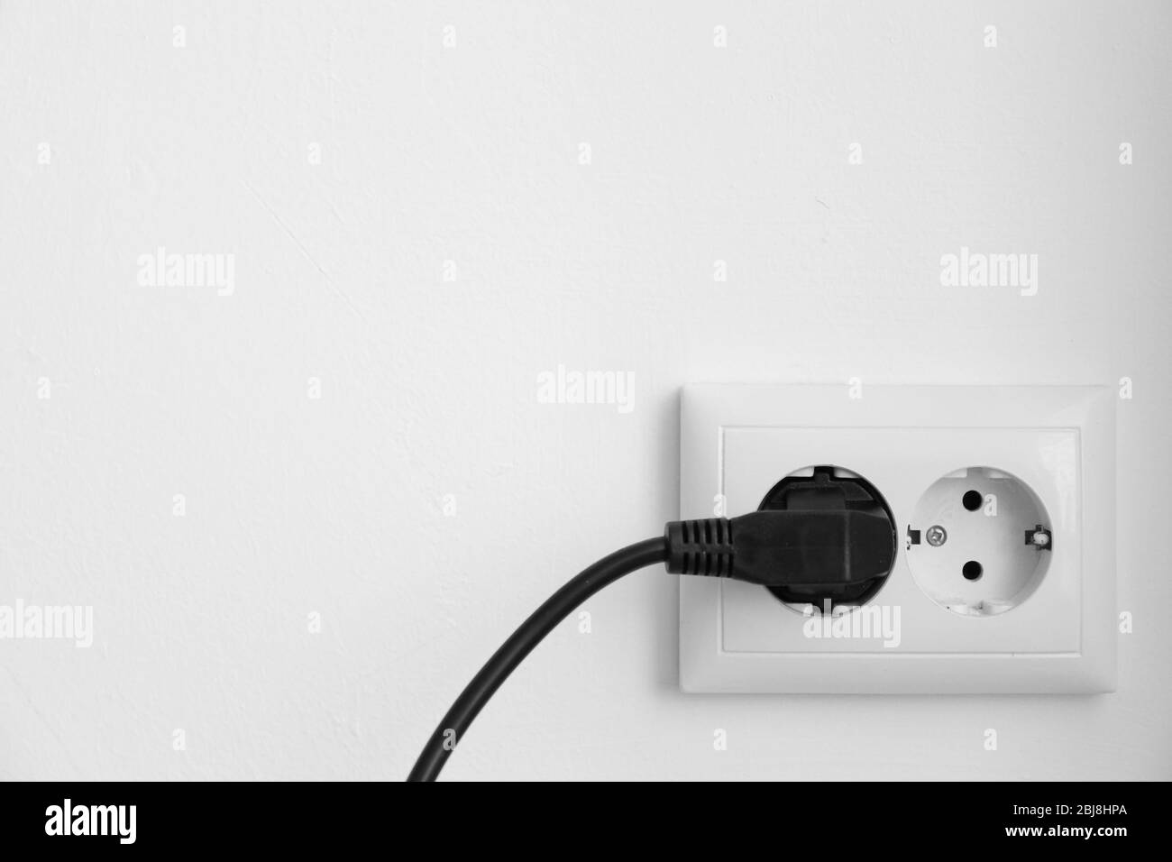 Schwarzer Netzstecker in Steckdose vor weißem Wandhintergrund Stockfoto