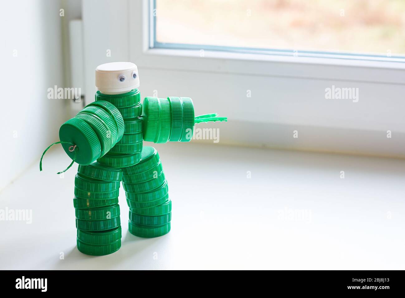 Recycling Kunst. Null Abfall, das zweite Leben der Dinge. Spielzeugroboter aus Plastikkappen am Fenster. Copyspace. Stockfoto