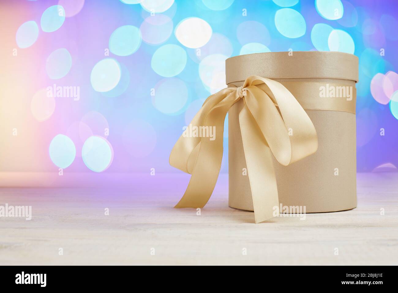 Geschenk runde Box mit Satinband Schleife auf verschwommenem Bokeh Hintergrund. Grußkarte oder Banner Copyspace. Stockfoto