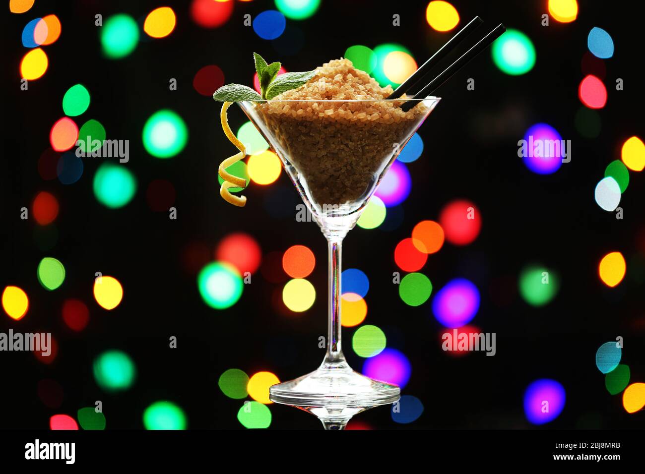 Martini-Glas mit braunem Granulatzucker auf dunklem Bokeh-Hintergrund Stockfoto