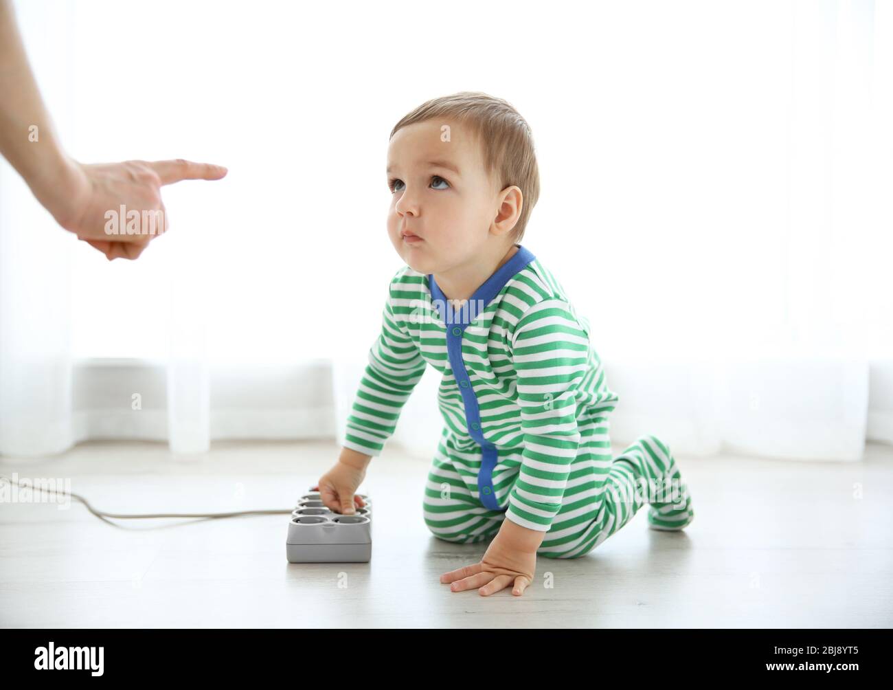 Mutter schimpft ihr Baby, das mit Stecker spielt Stockfoto
