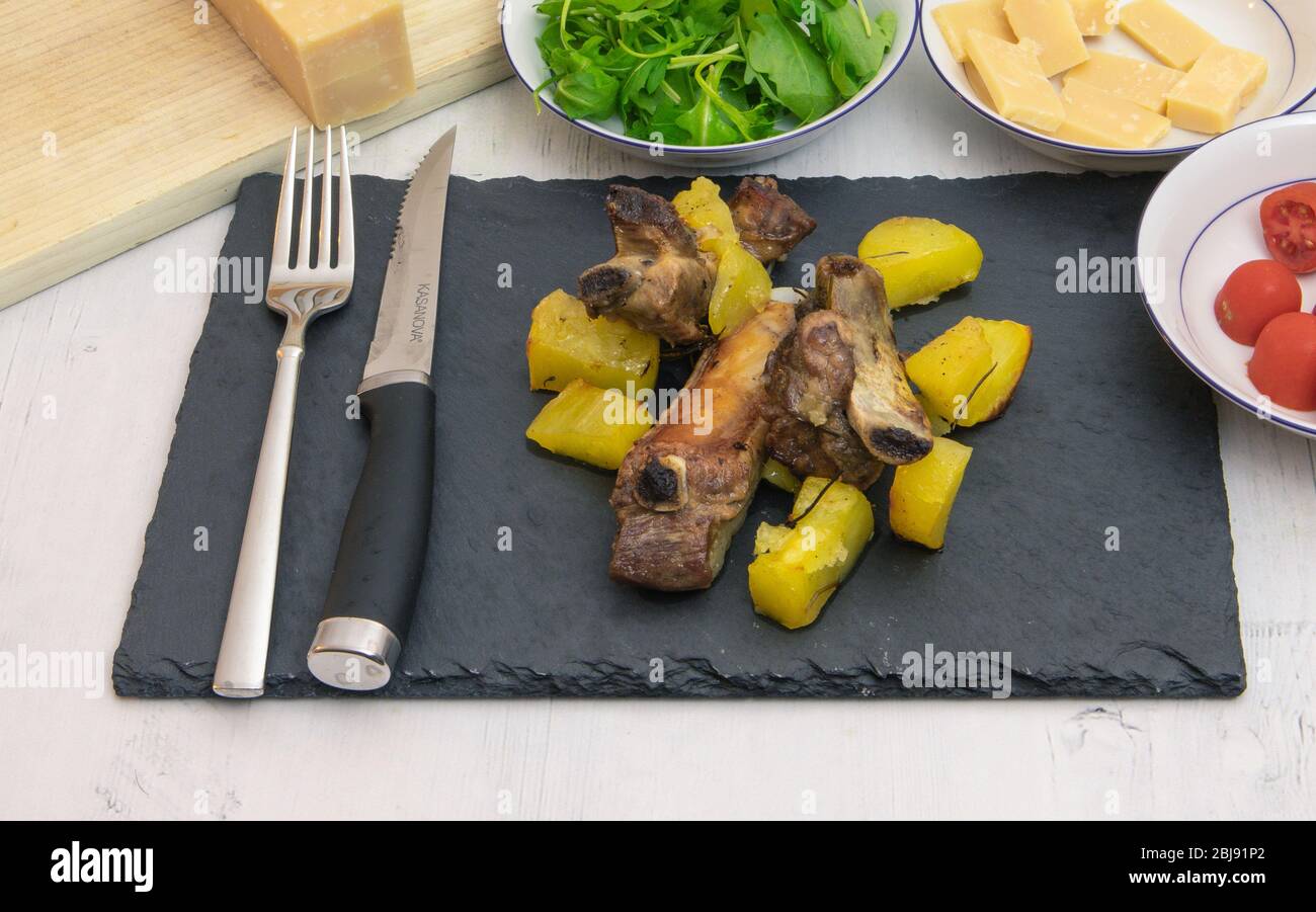 Gebackene Schweinerippchen mit Tomaten und Salat auf einem Schieferteller Stockfoto