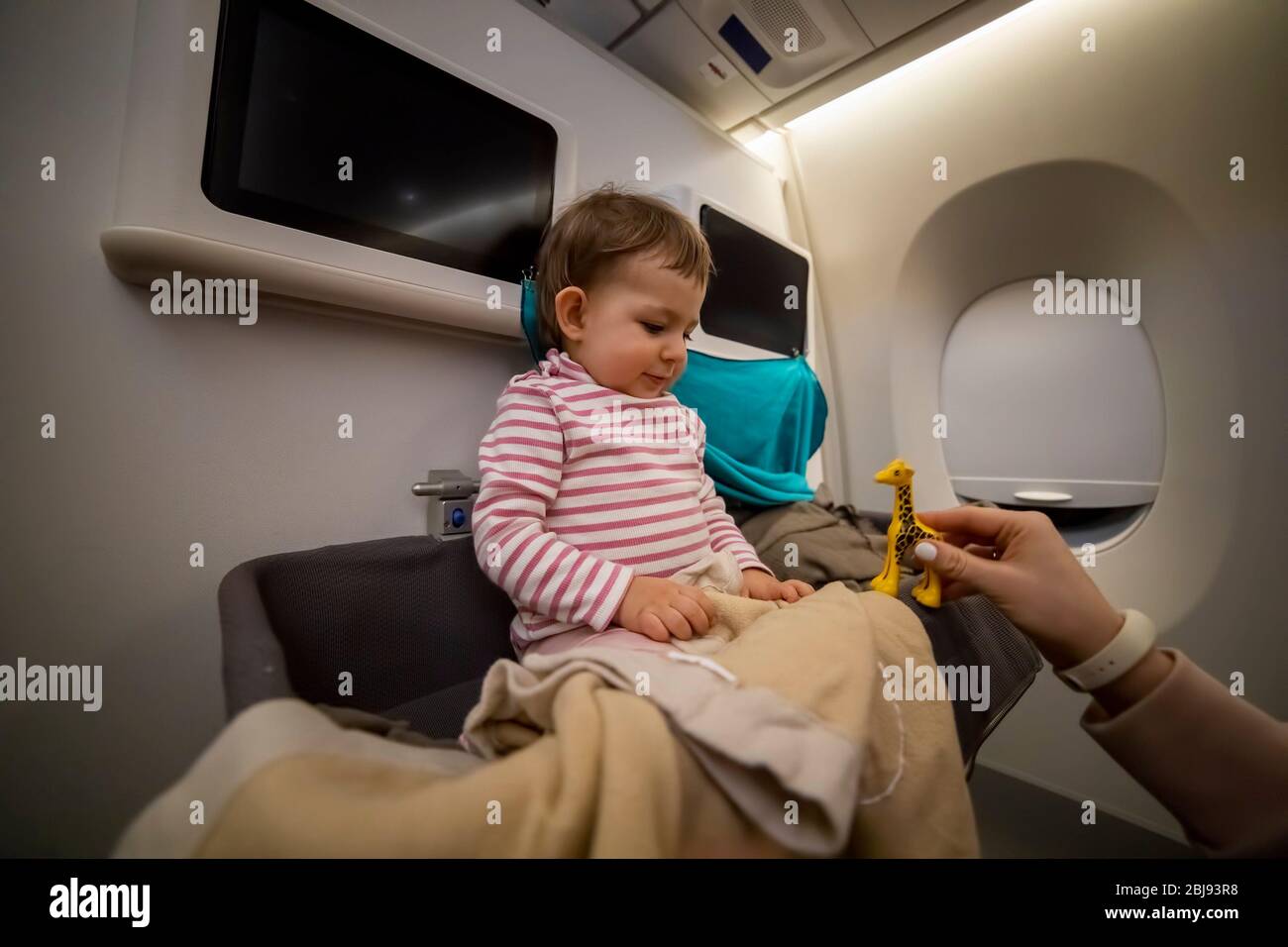 Mama Hand spielt ein Spielzeug mit einem glücklichen lächelnden kleinen niedlichen Kleinkind sitzt in der Babybinde eines Flugzeugs. Close-up, weiche Fokus. Stockfoto