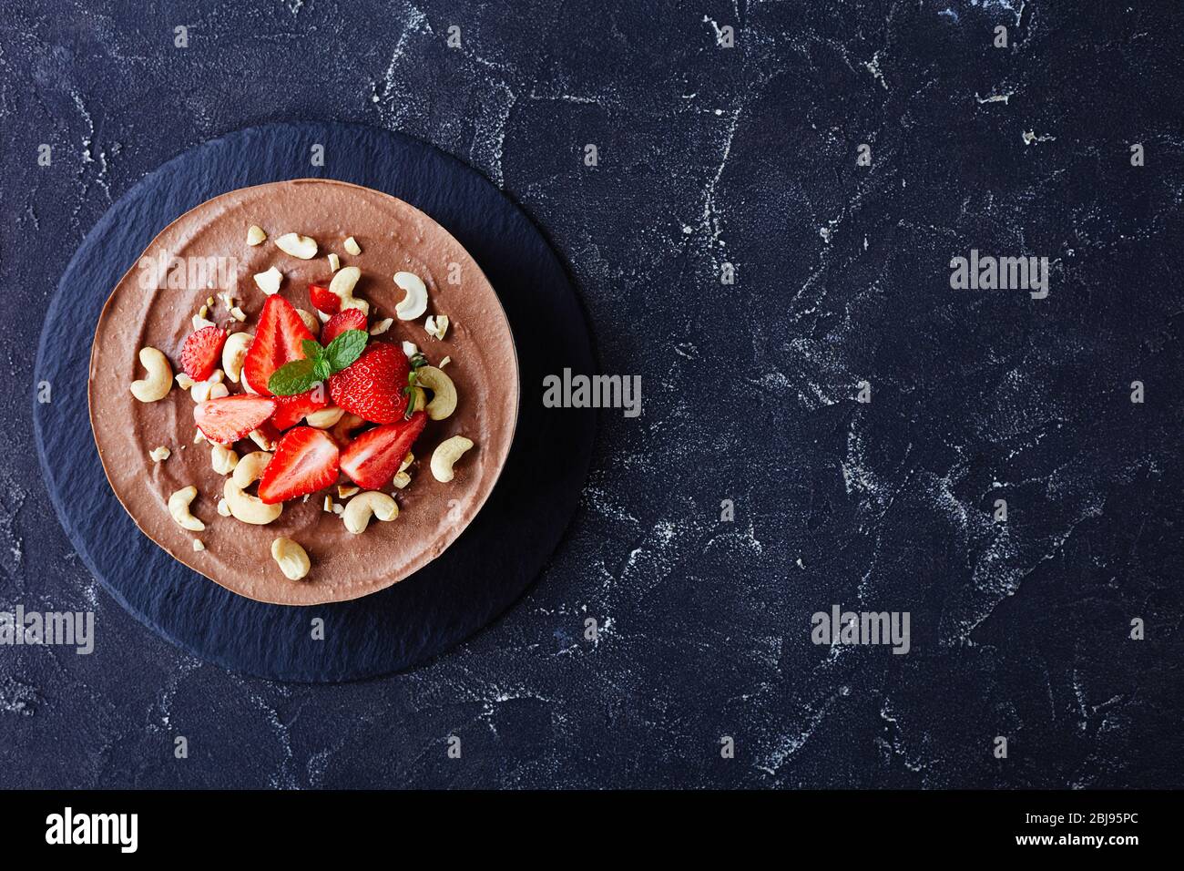 Pflanzenbasiert, nicht backen vegane Dessert Schokolade Käsekuchen mit No-Bake Kruste aus Datteln, Kakao und Pekannüsse mit Erdbeeren und Minze auf einem dunklen con Stockfoto