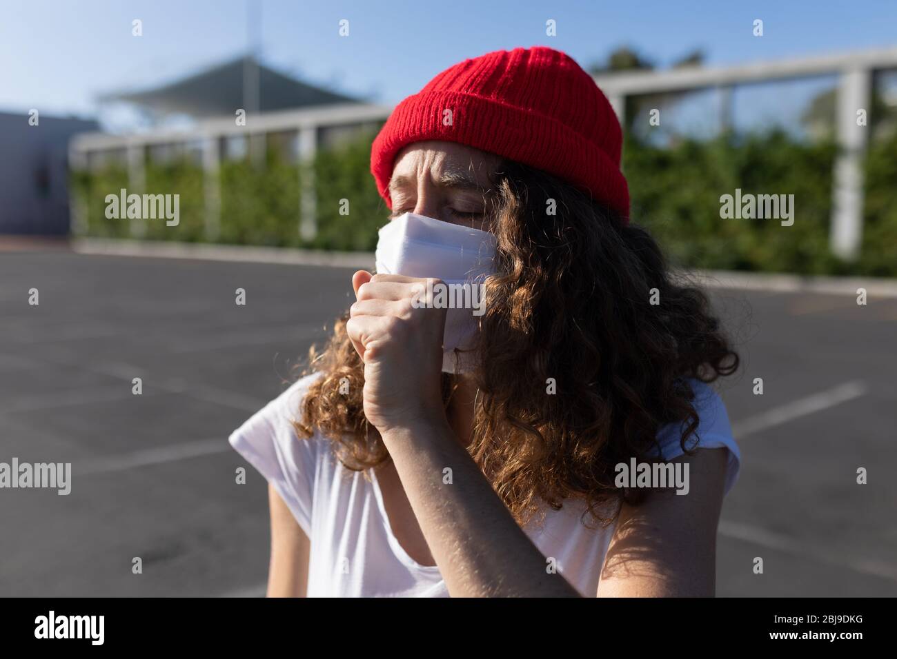 Kaukasische Frau mit einer Schutzmaske und hustet auf den Straßen Stockfoto