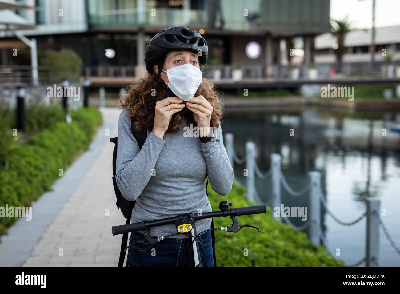Kaukasische Frau, die eine Schutzmaske aufsetzt und einen Fahrradhelm auf den Straßen trägt Stockfoto