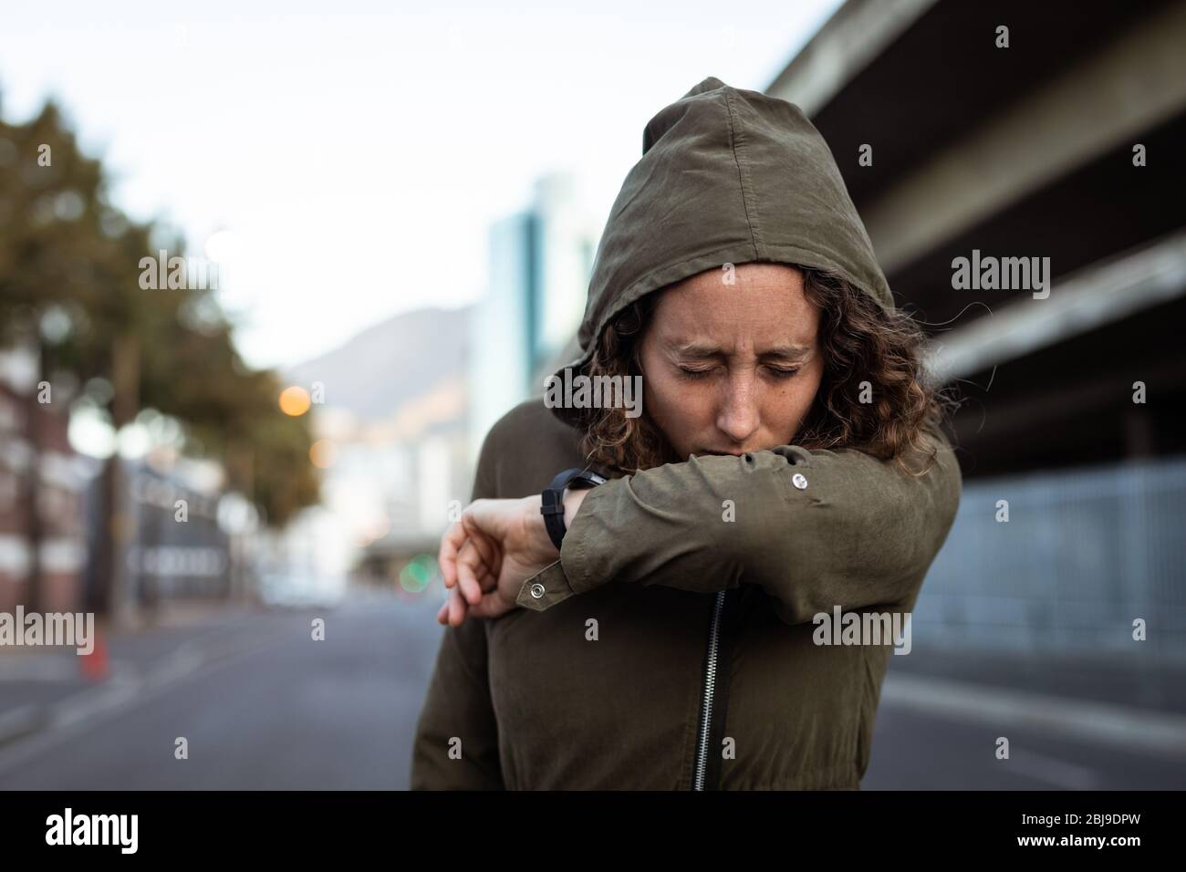 Kaukasische Frau hustet und trägt eine Smartwatch in den Straßen Stockfoto