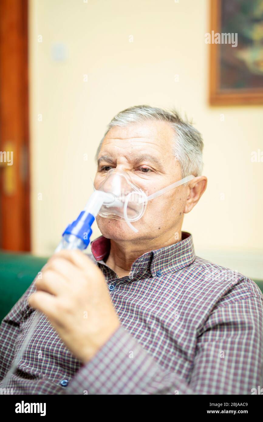 Leitender Mann, der medizinische Geräte für die Inhalation mit Atemschutzmaske verwendet, Vernebler im Zimmer Stockfoto