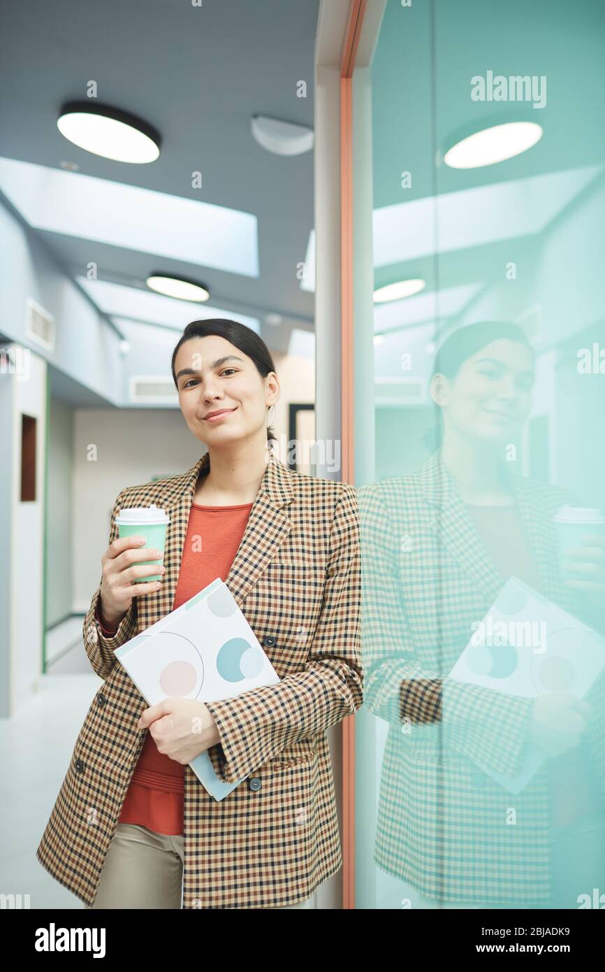 Porträt einer jungen Geschäftsfrau, die Dokument und eine Tasse Kaffee hält und die Kamera im Büro anschaut Stockfoto