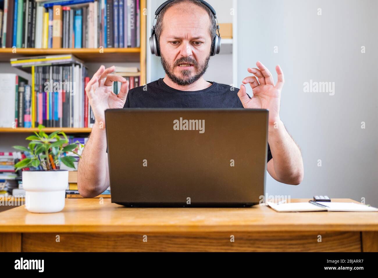 Mann, der von zu Hause aus arbeitet, auf Telekonferenz. Bärtiger Mann arbeitet online von zu Hause aus auf Computer-Laptop hinter Vintage-Schreibtisch mit Blume in Vase, mit Stockfoto