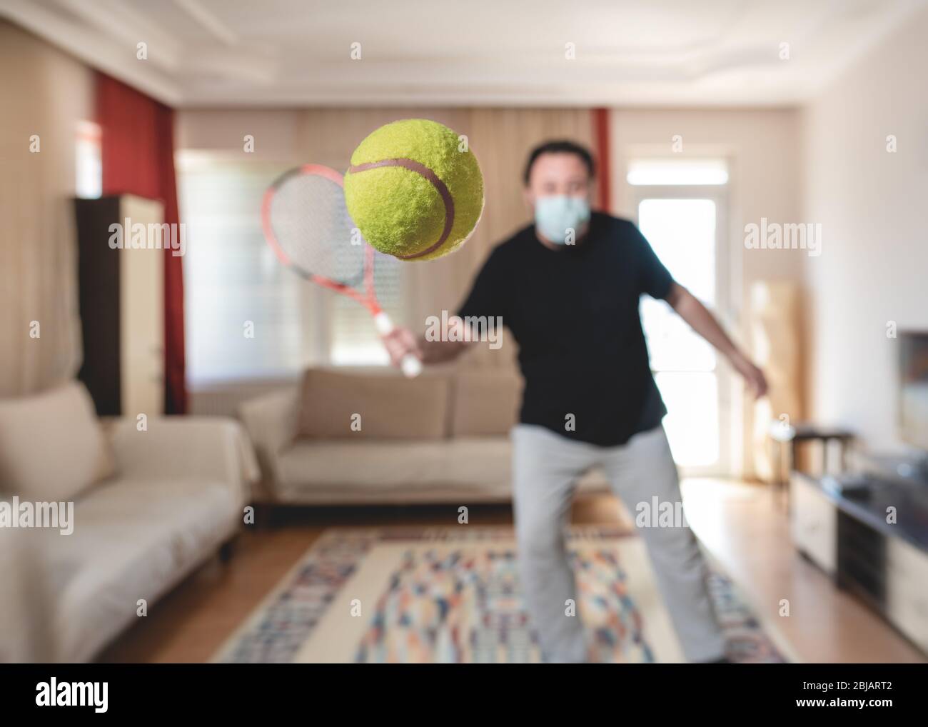 Mann mit schützender medizinischer Maske, der zu Hause Tennis in der Covid-19 Coronavirus-Ausbruchsquarantäne spielt. Stockfoto