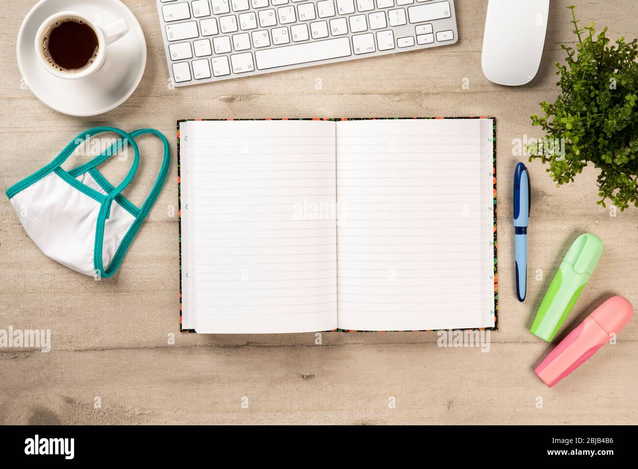 Büroarbeitsplatz mit Tastatur, Handy, Notebook, Kaffee und einer Schutzmaske gegen Corona-Virus und andere Schreibwaren auf Holzhintergrund Stockfoto