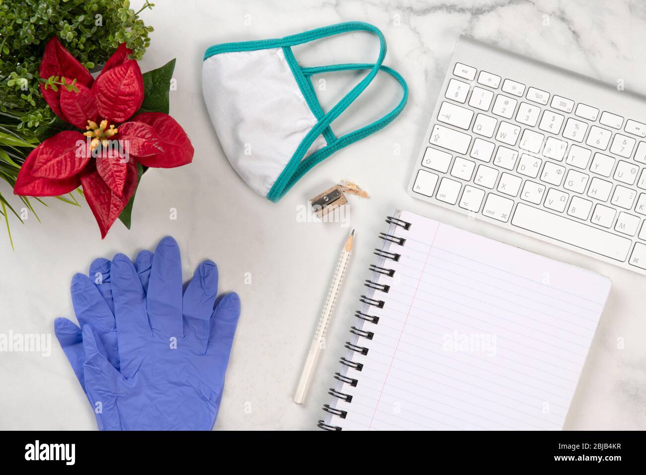 Ärzte Schreibtisch mit Schutzmaske und Handschuhen gegen das Corona-Virus, ein Notizbuch, einen Bleistift, eine rote Blume und eine Tastatur auf einem Schreibtisch mit Marmorstruktur Stockfoto