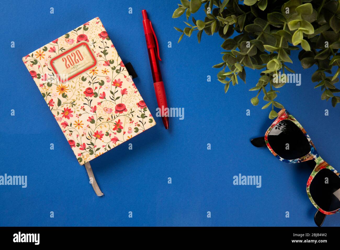 Blauer Schreibtisch mit buntem Tagebuch, Sonnenbrille und grüner Pflanze. Konzept von oben Stockfoto