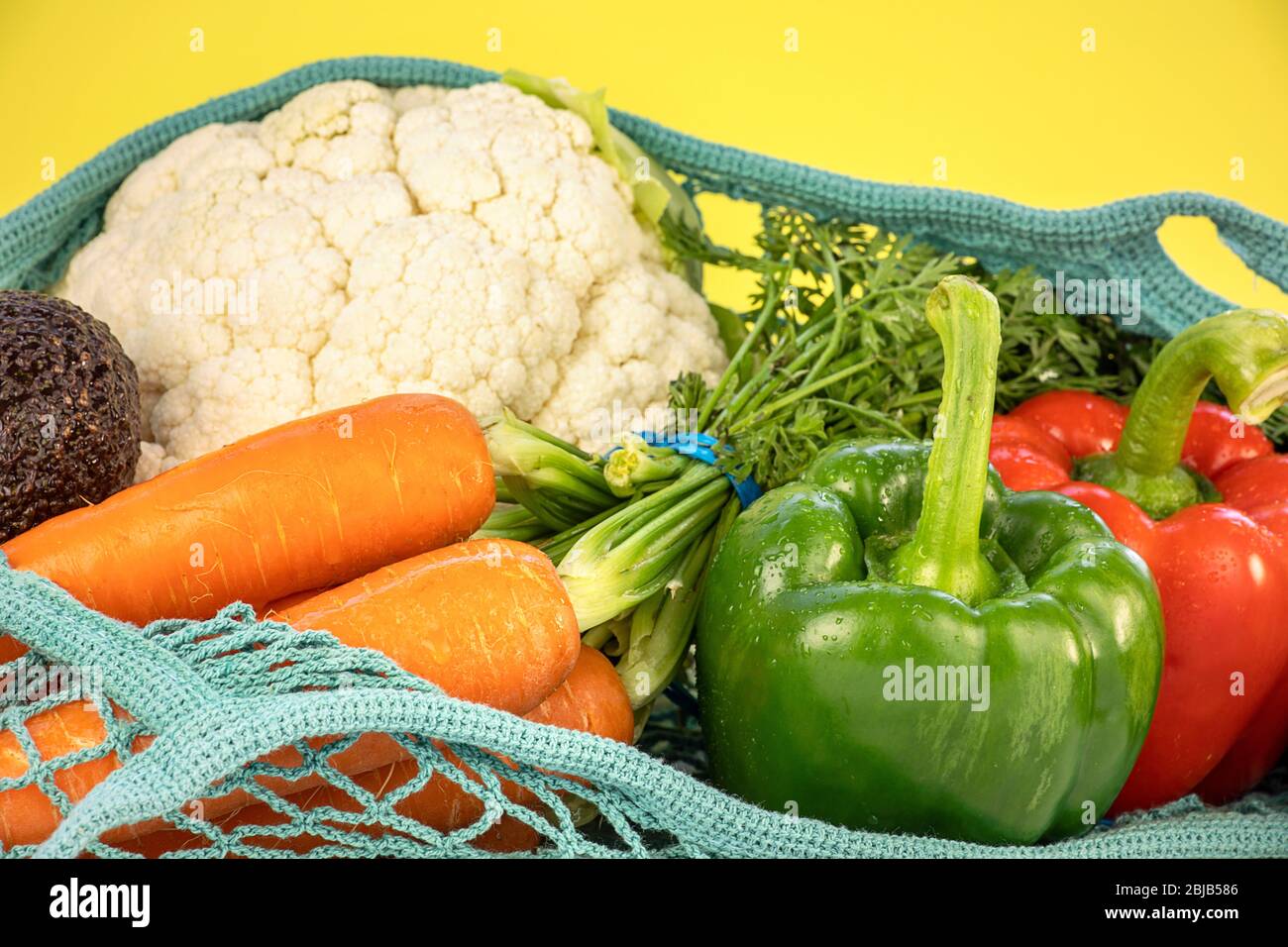 Nahaufnahme von frischem Gemüse in Netzbeutel, auf gelbem Hintergrund, bunte Zusammensetzung. Verschiedene Gemüse Anordnung, gesundes Essen Konzept. Stockfoto