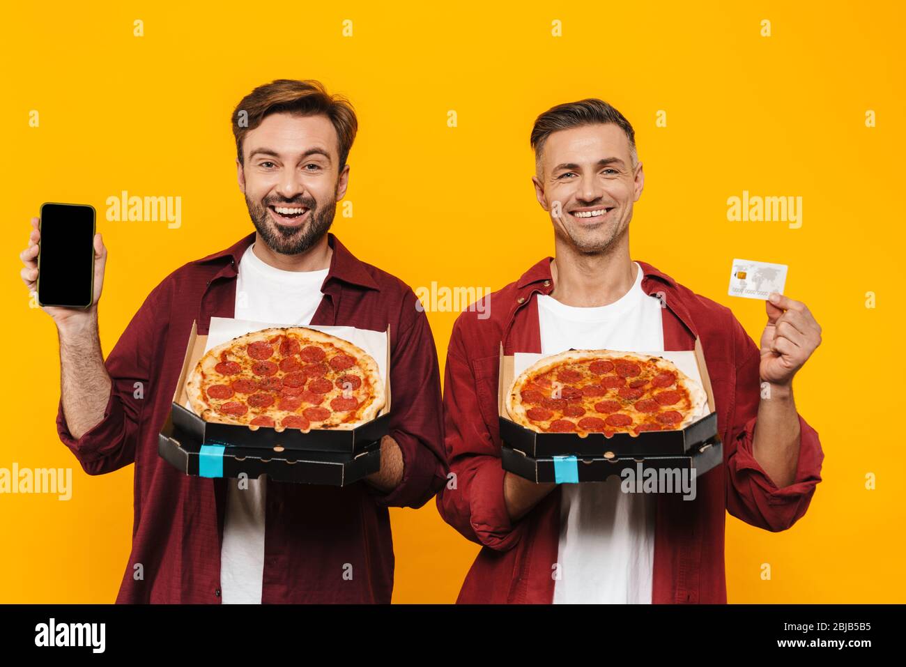 Zwei attraktive fröhlich aufgeregt jungen Männern Freunde in lässigen Kleidung stehen isoliert über gelben Hintergrund, zeigt leere Handy und Cred Stockfoto