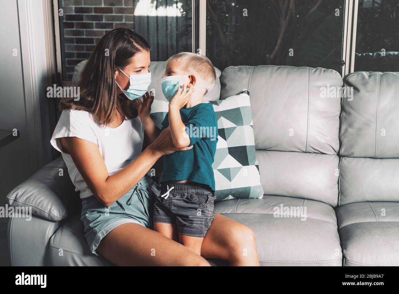 Mutter und Kind tragen Facemask während des Coronavirus- und Grippeausbruchs zu Hause. Virenschutz. Mutter und Sohn versuchen, die Ausbreitung der Krankheit zu stoppen. Stockfoto
