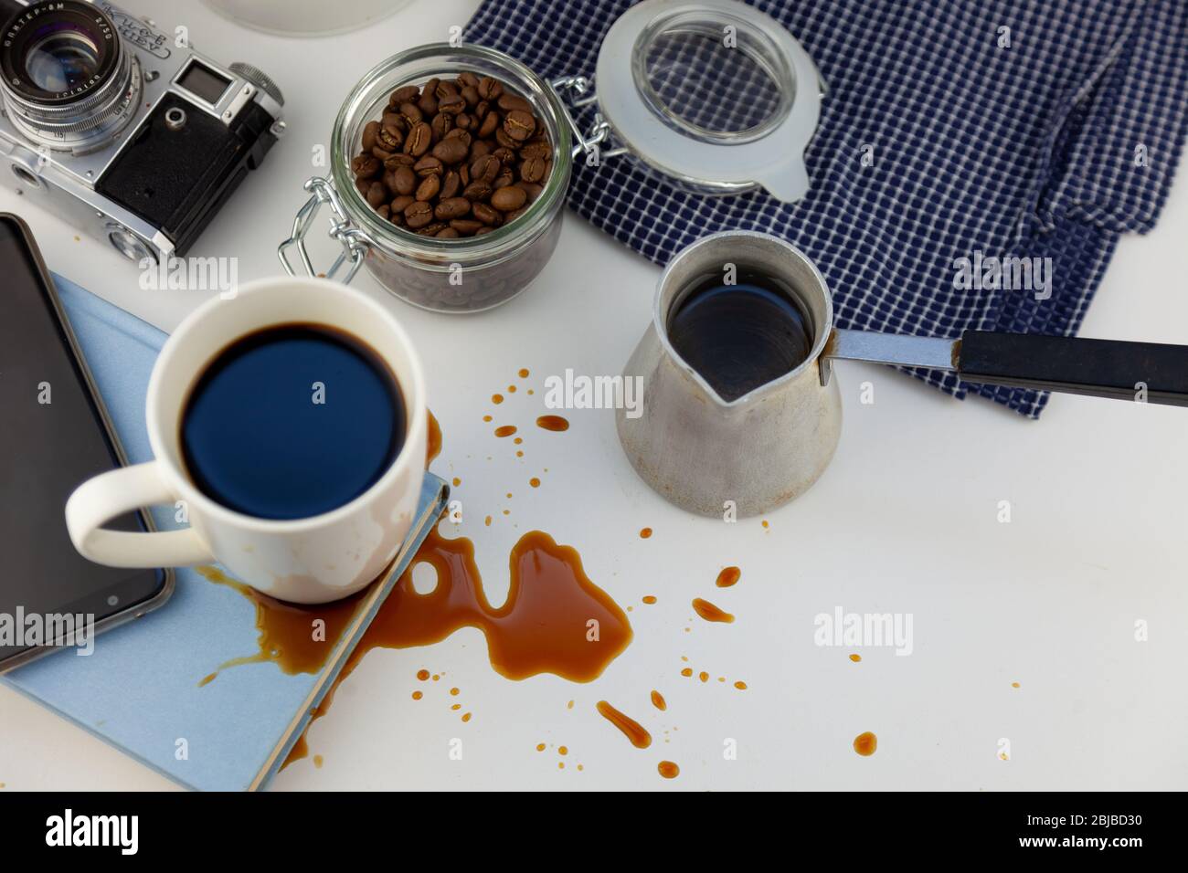 Kaffee verschüttet auf einem Buch auf dem Desktop. Ein cezve für Kaffee,  Kaffeebohnen, eine weiße Tasse Kaffee, verschütten ein Getränk auf den  Tisch, eine Pfütze und Stockfotografie - Alamy