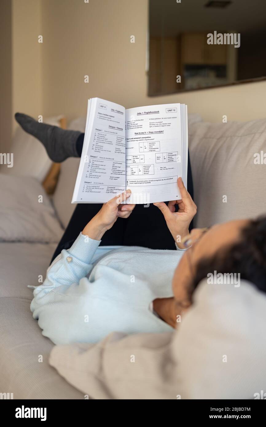 Hübsche spanische Frau auf dem Sofa sitzend, Englisch zu Hause lernend Stockfoto