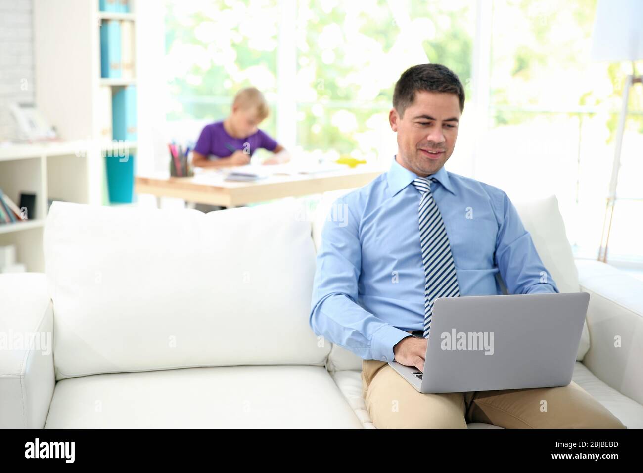 Vater arbeitet mit Laptop und sein Sohn Zeichnung auf Hintergrund Stockfoto