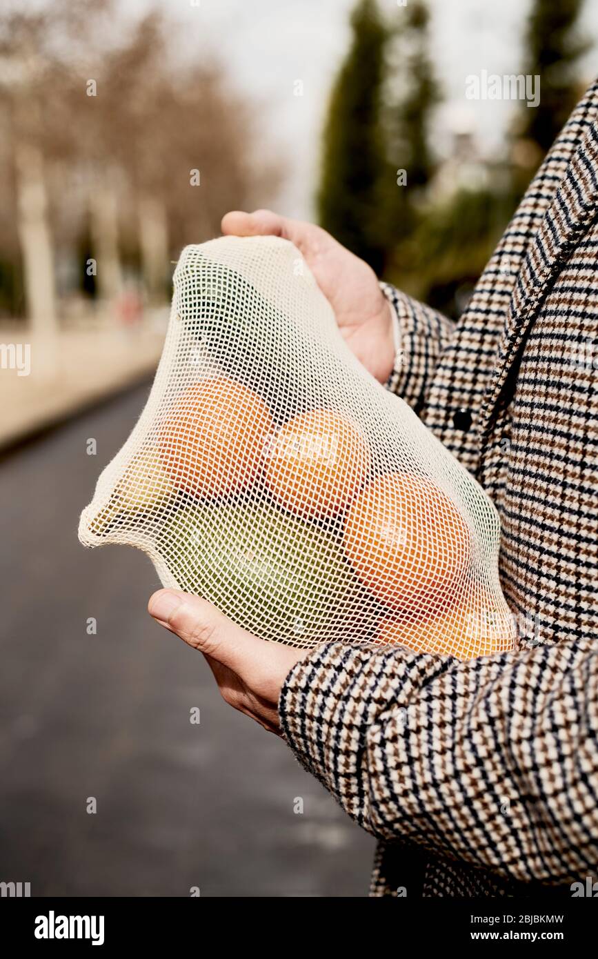 Nahaufnahme eines Mannes auf der Straße mit einem textilen wiederverwendbaren Netzbeutel, verwendet, um Lebensmittel in großen Mengen zu kaufen, voll von Obst und Gemüse, als Maßnahme zu rot Stockfoto