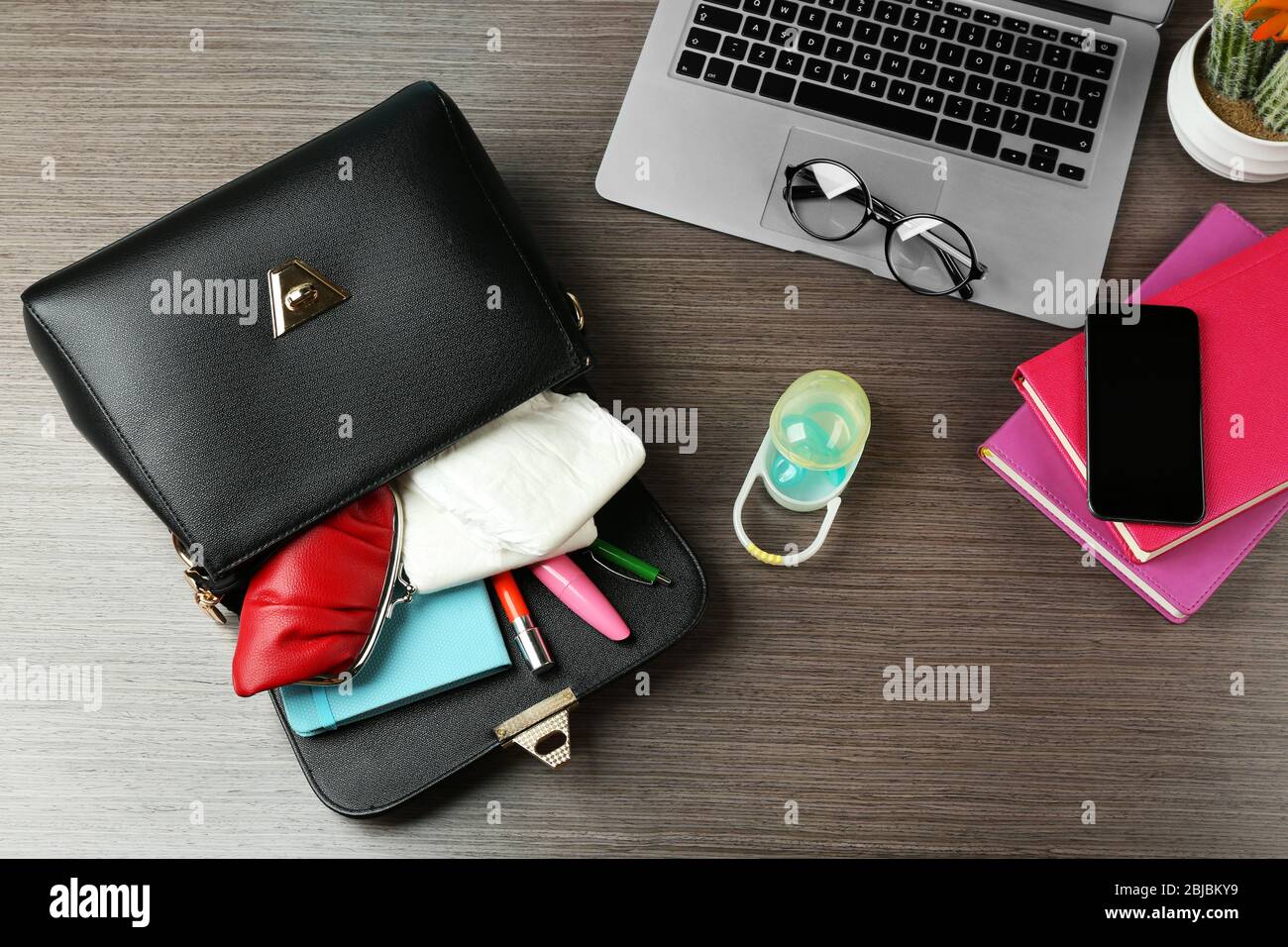 Mutterschaftskonzept. Weibliche Handtasche voller verschiedener Dinge auf dem Bürotisch Stockfoto