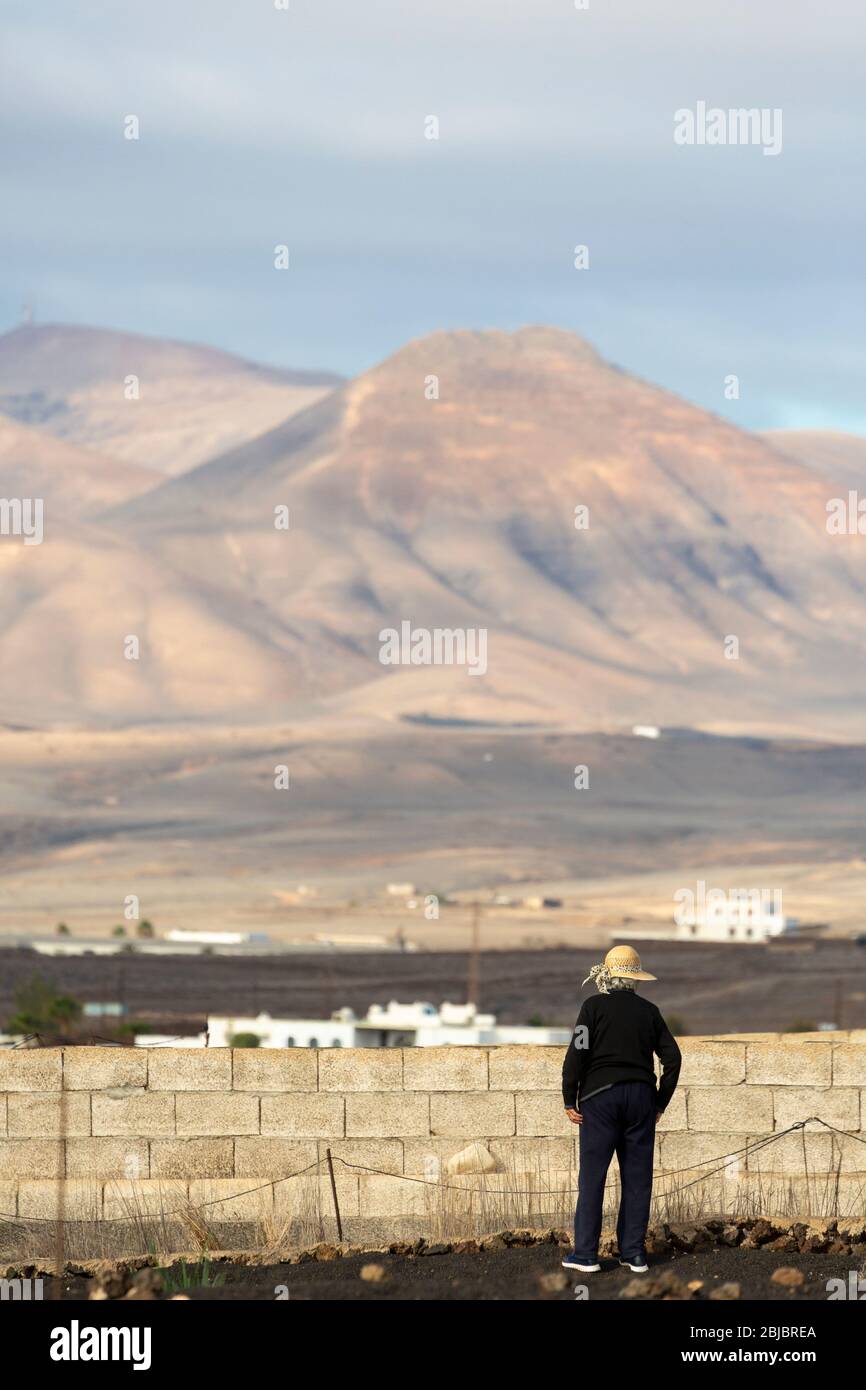 Eine einheimische Frau arbeitet vor ihrem Haus mit vulkanischer Landschaft im Hintergrund, Lanzarote, Kanarische Inseln, Spanien Stockfoto