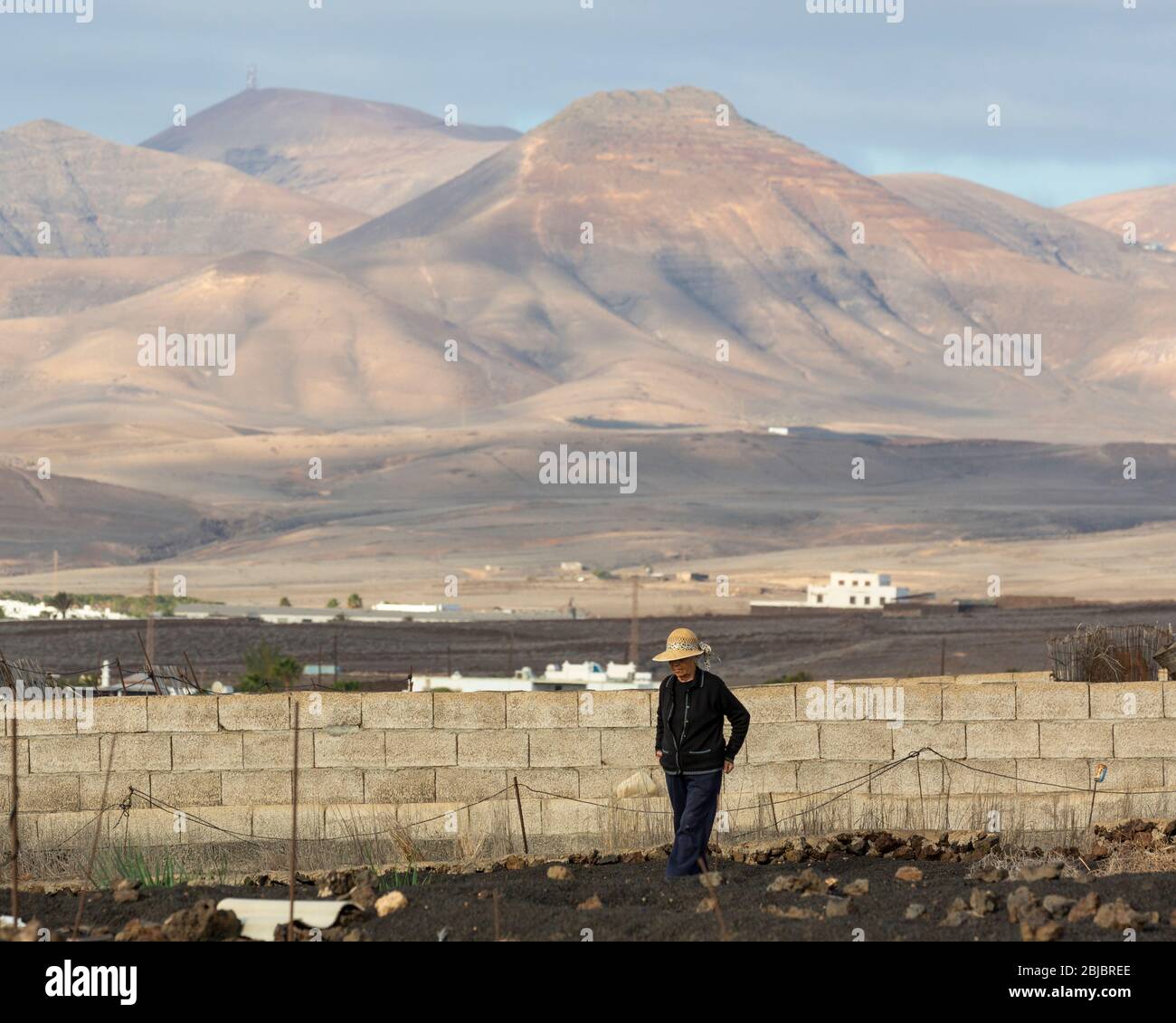 Eine einheimische Frau arbeitet vor ihrem Haus mit vulkanischer Landschaft im Hintergrund, Lanzarote, Kanarische Inseln, Spanien Stockfoto