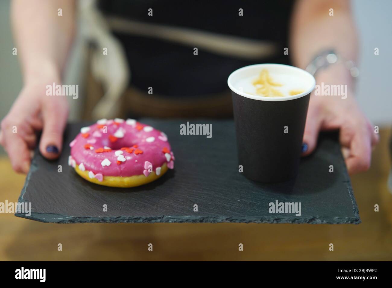 Der Barista hält ein Tablett mit Donut und Kaffee. Stockfoto