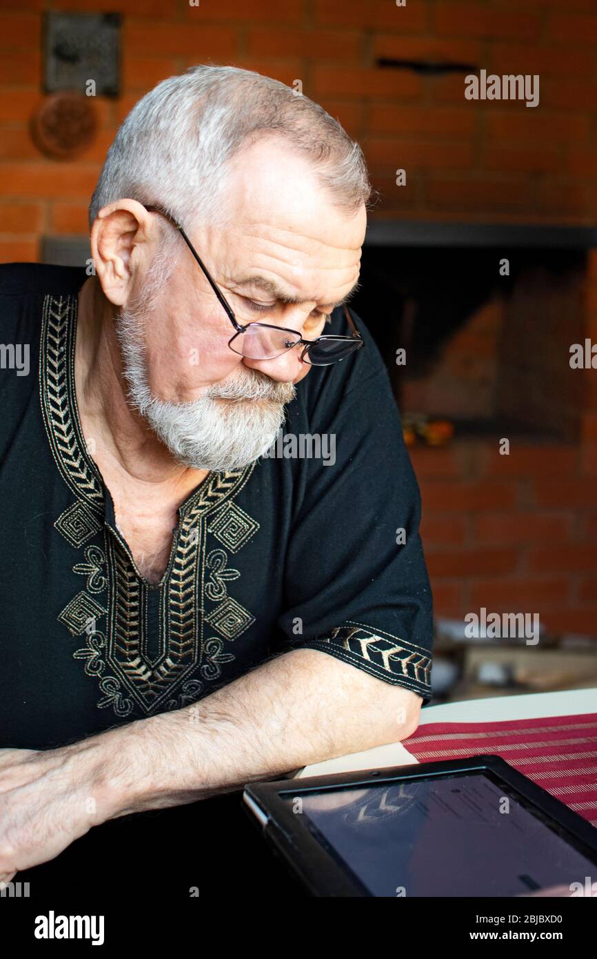 Senior Mann arbeitet mit Tablet zu Hause. Ein Mann mit Brille studiert neue Technologien. Stockfoto